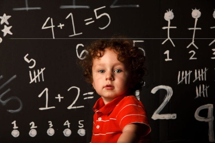 A child in front of a blackboard with math problems on it