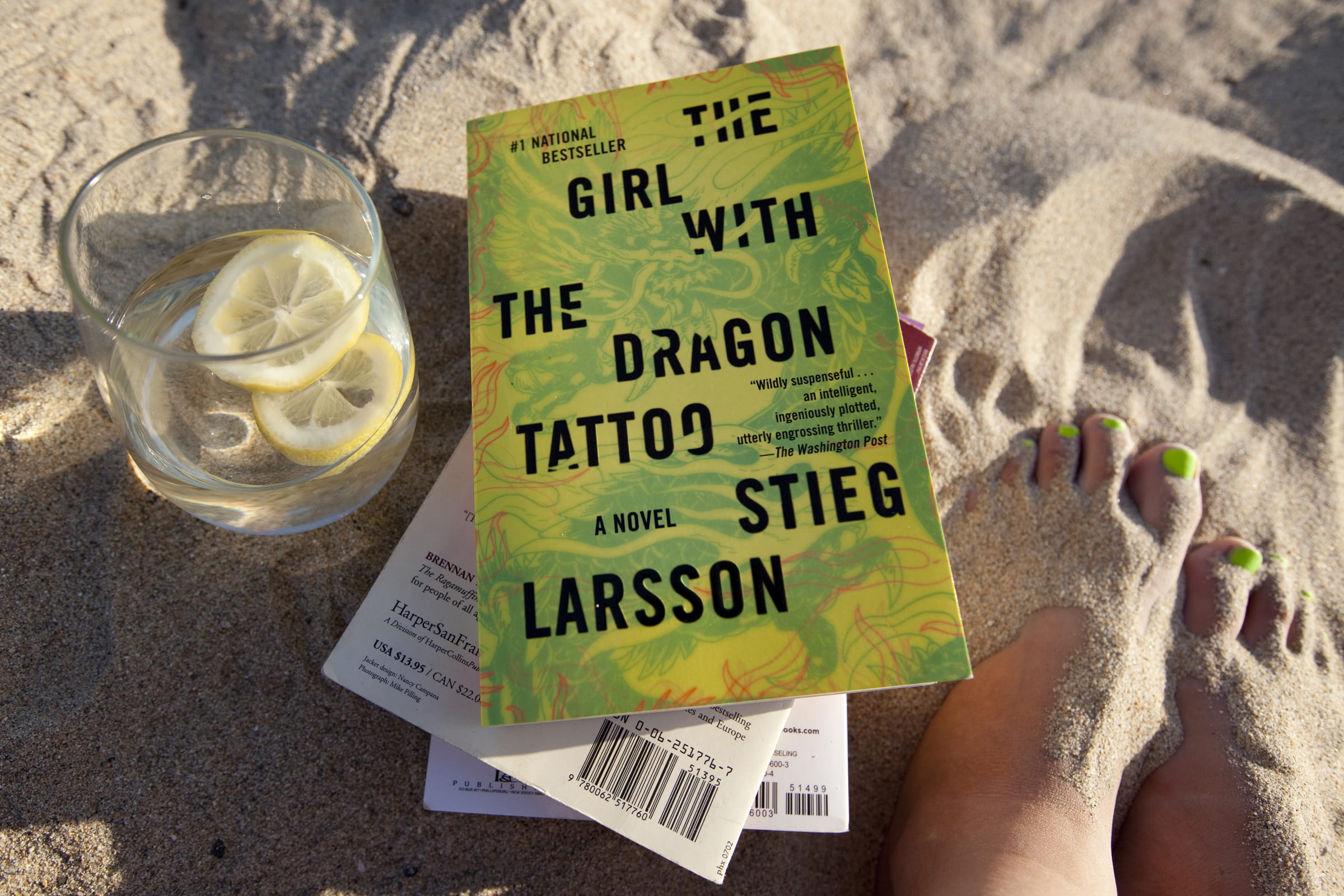 "Girl With The Dragon Tattoo" book sitting in the sand