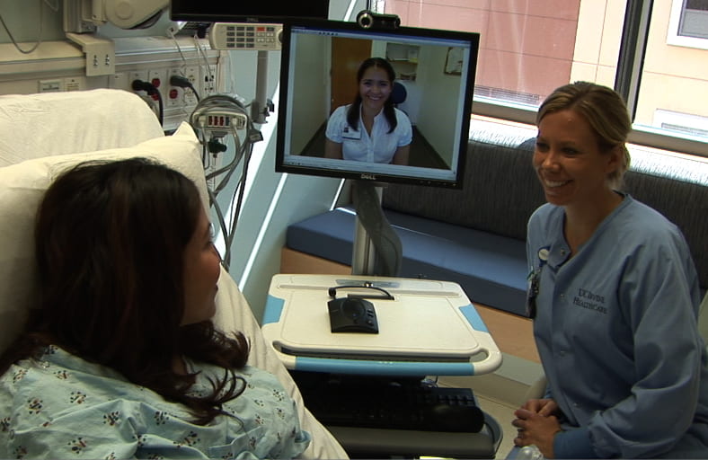Gloria Guzman, on the monitor, translates for nurse Danielle Lawson and a patient