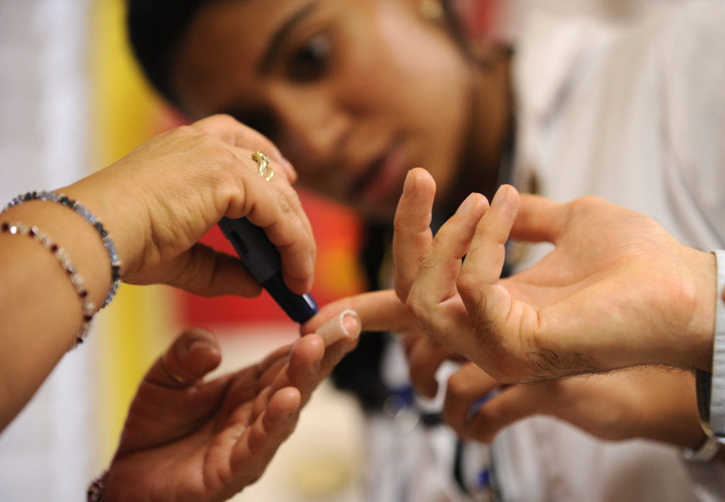 Medical students help a patient practice pricking a finger as part of blood sugar test.