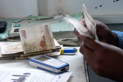 A Kenyan man completes transactions in cash and by cell phone.