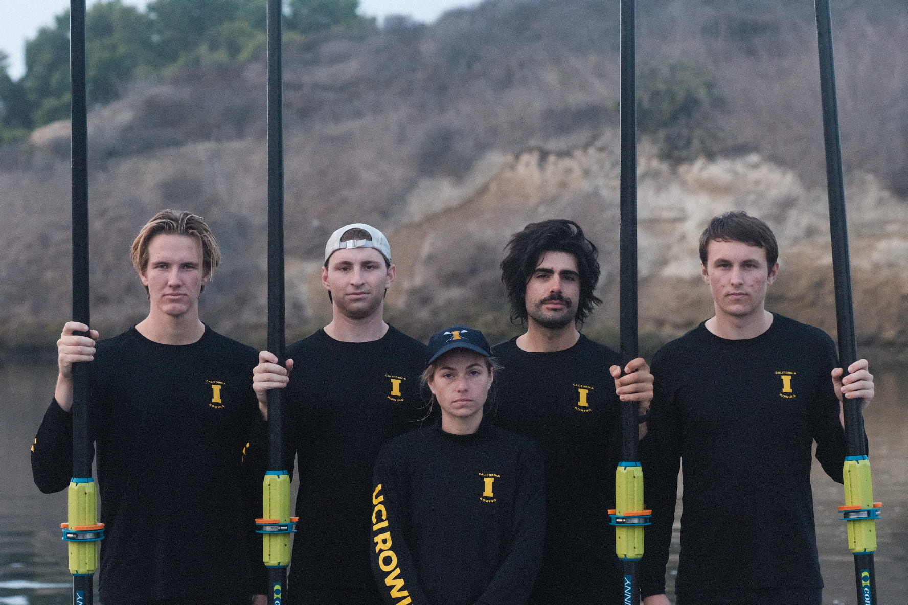 Five student athletes standing with rowing paddles