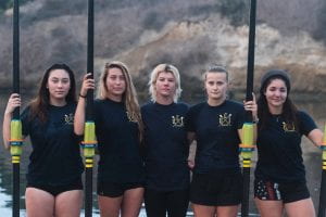 five female student athletes standing with their rowing paddles 