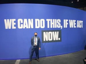 Micheal Mendez, UCI assistant professor of urban planning & public policy, at the 2021 U.N. Climate Change Conference standing in front of a sign that says, "We can do this, if we act now."