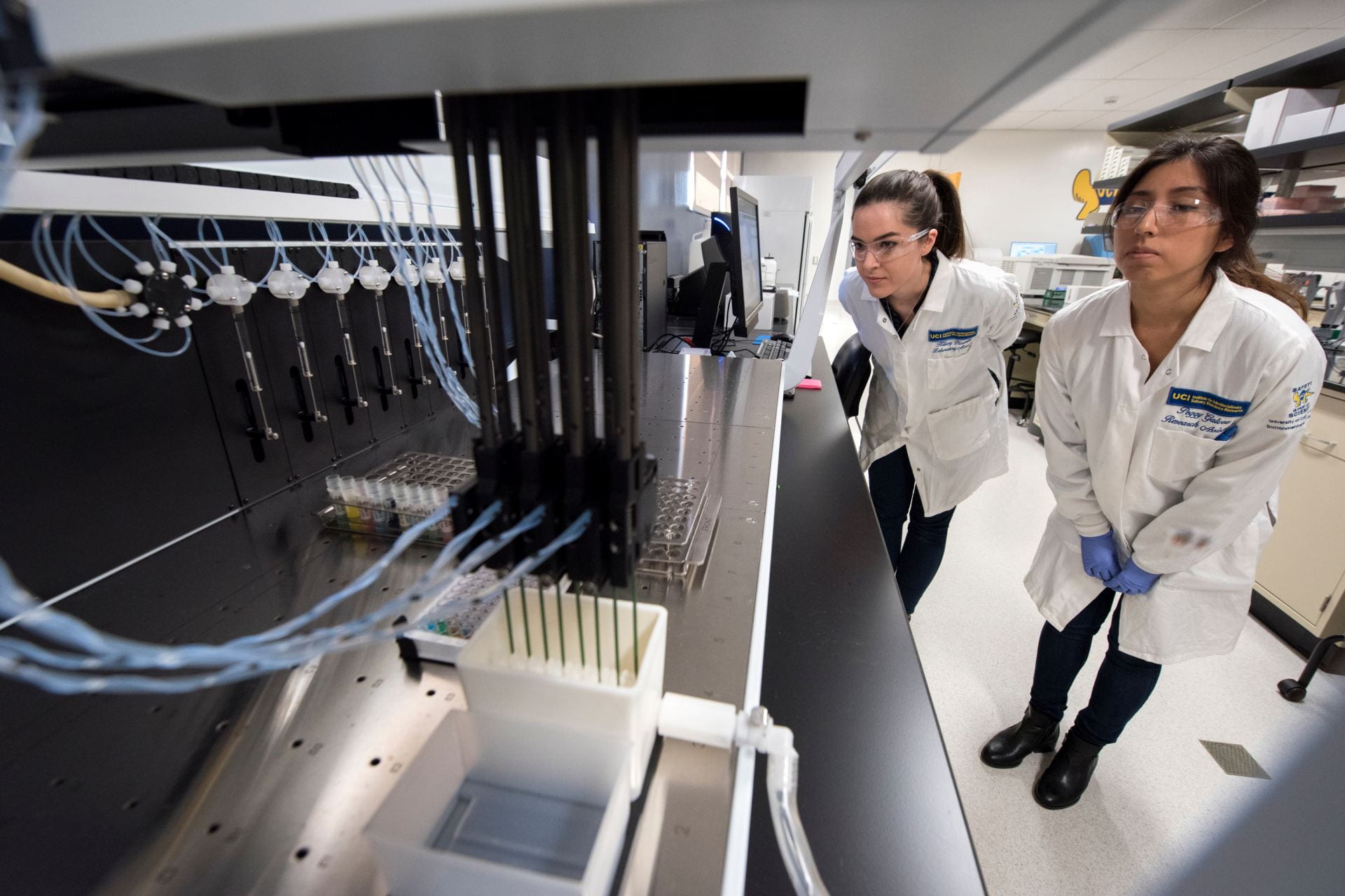 Institute for Interdisciplinary Salivary Bioscience Research laboratory manager Hillary Piccerillo (left) and former lab technician Peggy Galvez oversee the robotic transfer of saliva from collection tubes to test plates for an experiment.