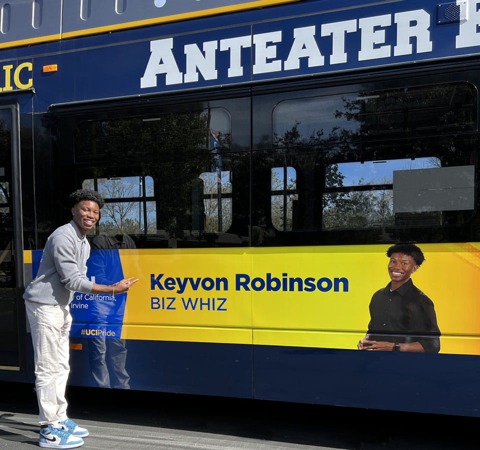 Student Keyvon Robinson stands next to his banner displayed on the Anteater Express bus