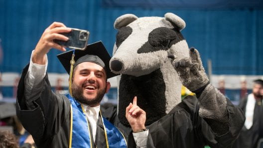Man in cap and gown standing with UCI mascot, Peter the Anteater.