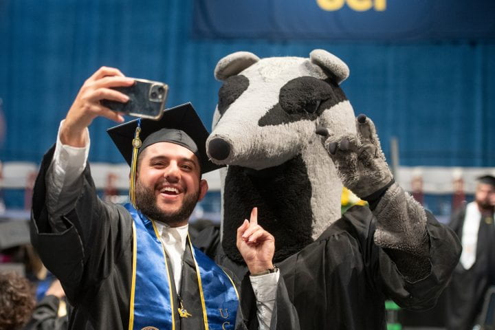 Man in cap and gown standing with UCI mascot, Peter the Anteater.