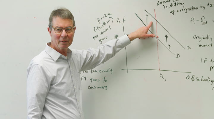 Greg J. Duncan, UCI Distinguished Professor of education points to a graph on a white board.