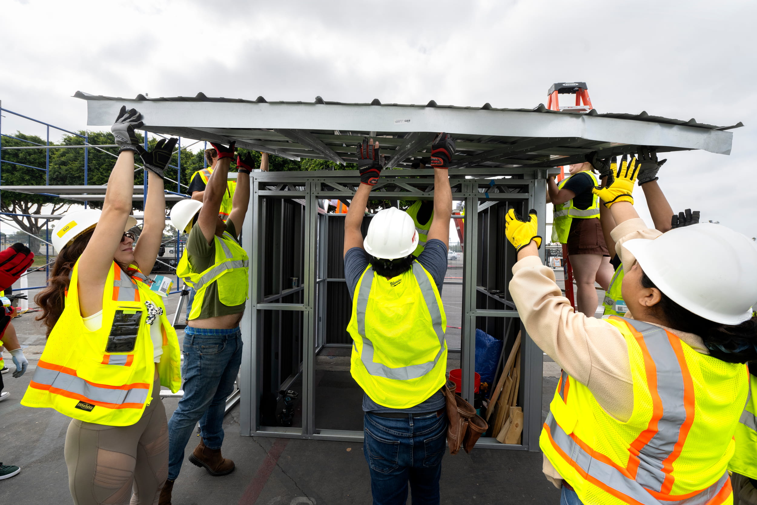 Workers in hard hats and yellow vests work together to place a roof frame on top of a structure.