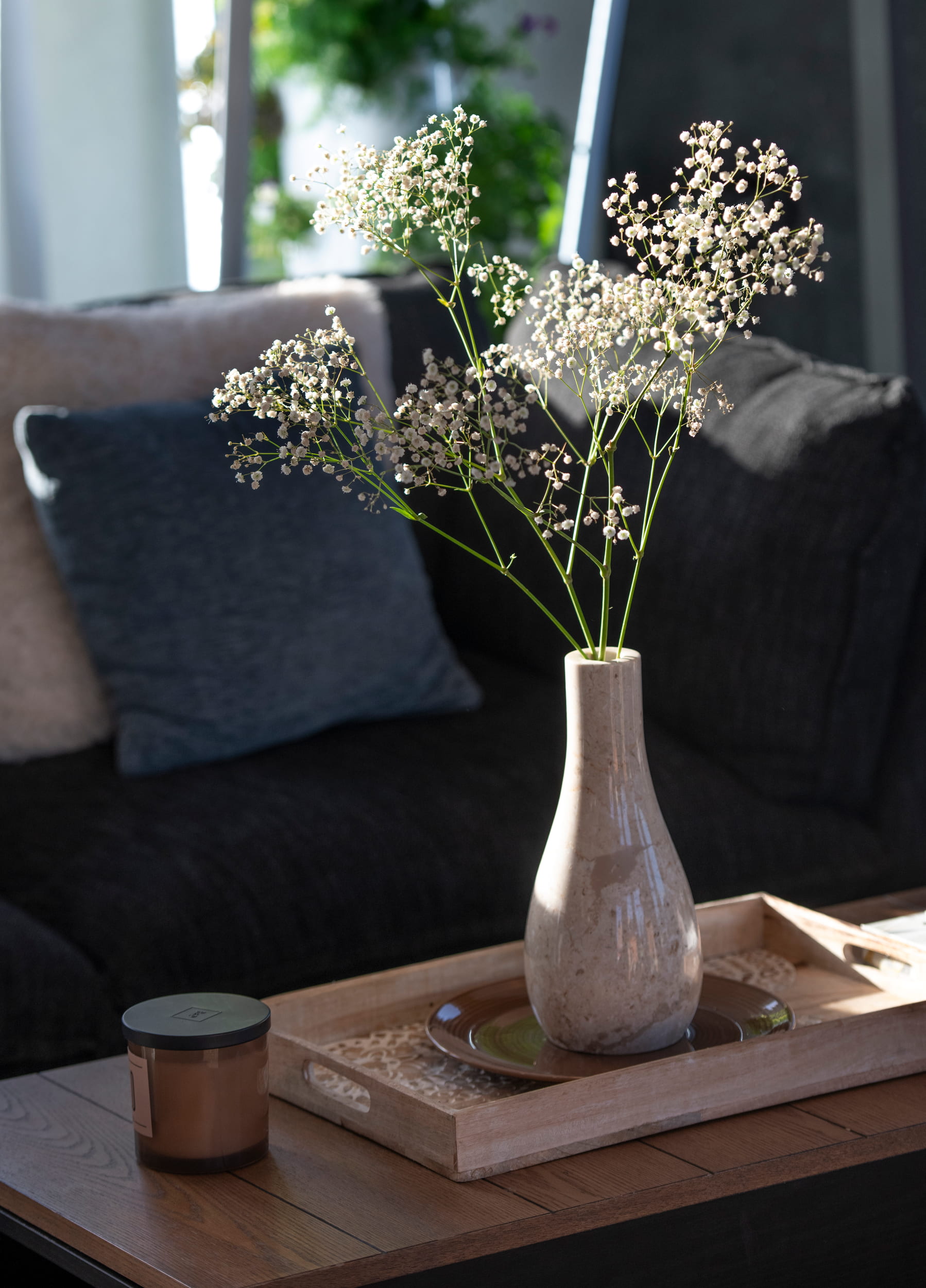 A decorative vase with baby's breath flowers on a coffee table in front of a sofa.