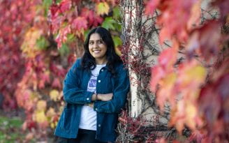 UCI informatics major Shalini Bhakta leaning against building with leaves in the backgroundl