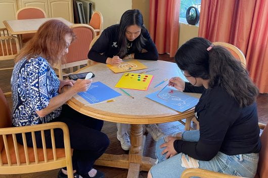 Patient Project volunteers work on an arts-and-crafts activity with a resident at Irvine’s Inn at Woodbridge senior living community.
