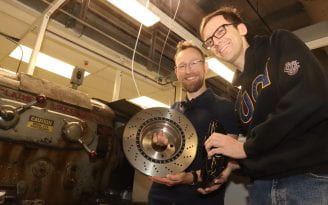 Lead study authors Adam Thomas (right) and Paulus Bauer (left) hold a brake rotor and caliper next to the lathe they and their UCI team used to measure car brake emissions.