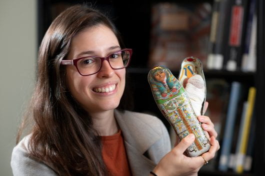Luiza Osorio G. Silva, a UC Irvine assistant professor of art history holding a replica coffin and a homemade mummy she has owned since childhood.