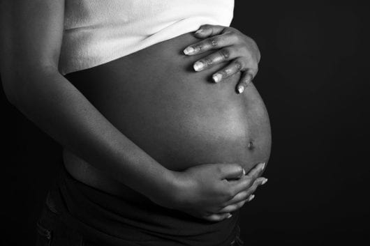 A pregnant African woman holding her belly on dark background.