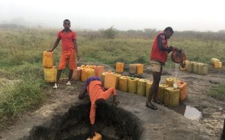 Three men collecting water from an open well