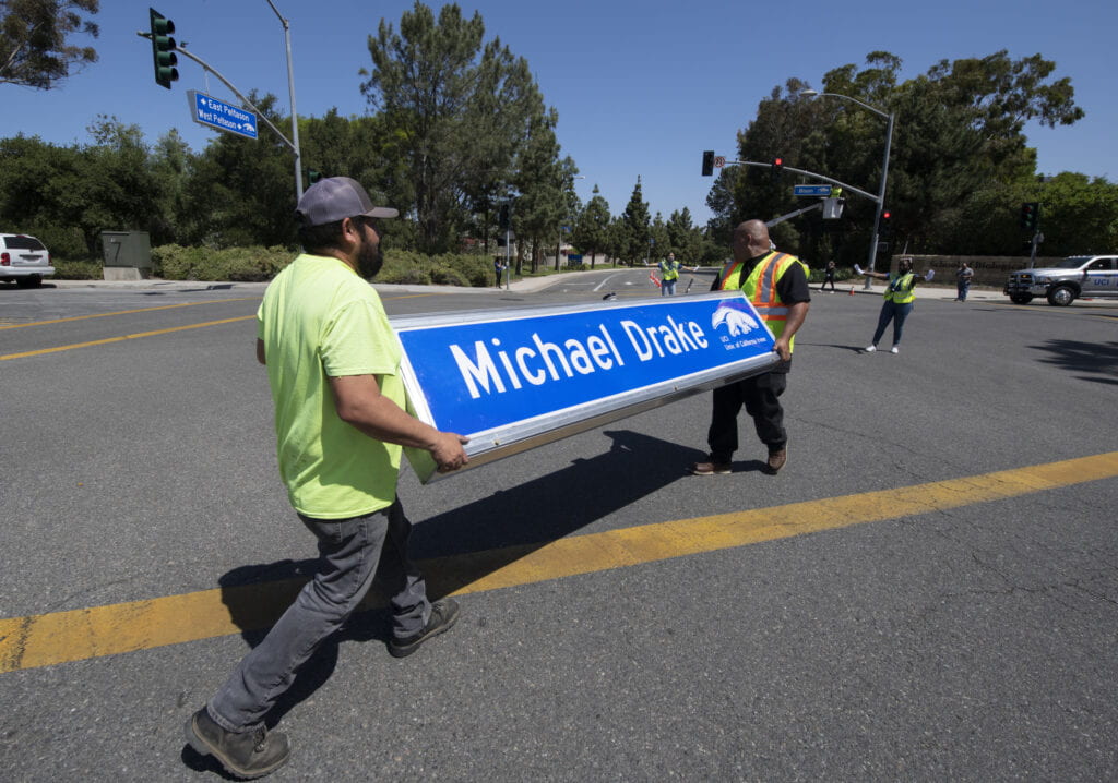 Two men carrying a street sign that says Michael Drake,